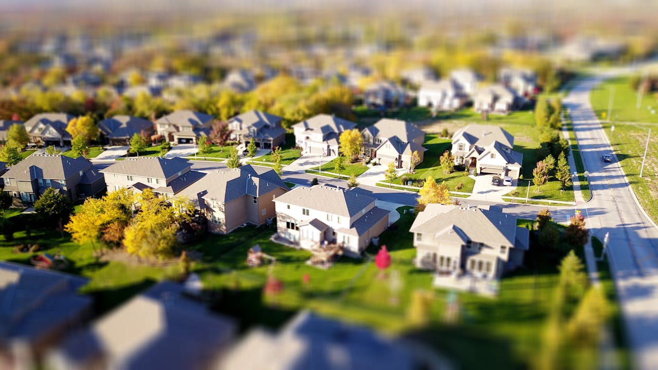 gallery-04 Tilt-shift aerial photo of a suburban neighborhood with green lawns and roads.